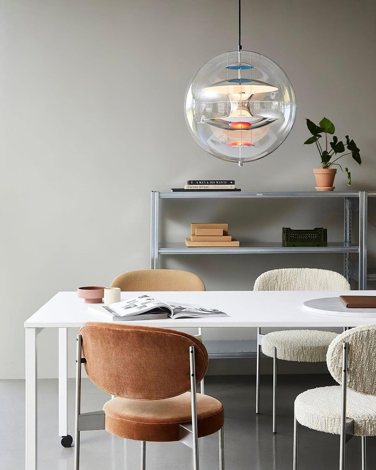 A Clérachic sphere pendant hangs above a white desk with a velvet chair, boucle stools and a metal shelving unit behind.