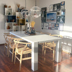 Two Clérachic sphere pendants hang above a white table in a sunny room with a gallery wall, cube shelves and wishbone chairs.