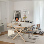 This Clérachic sphere pendant hangs in a pale room above an oval table with a cane chair, a framed portrait and a cream rug.