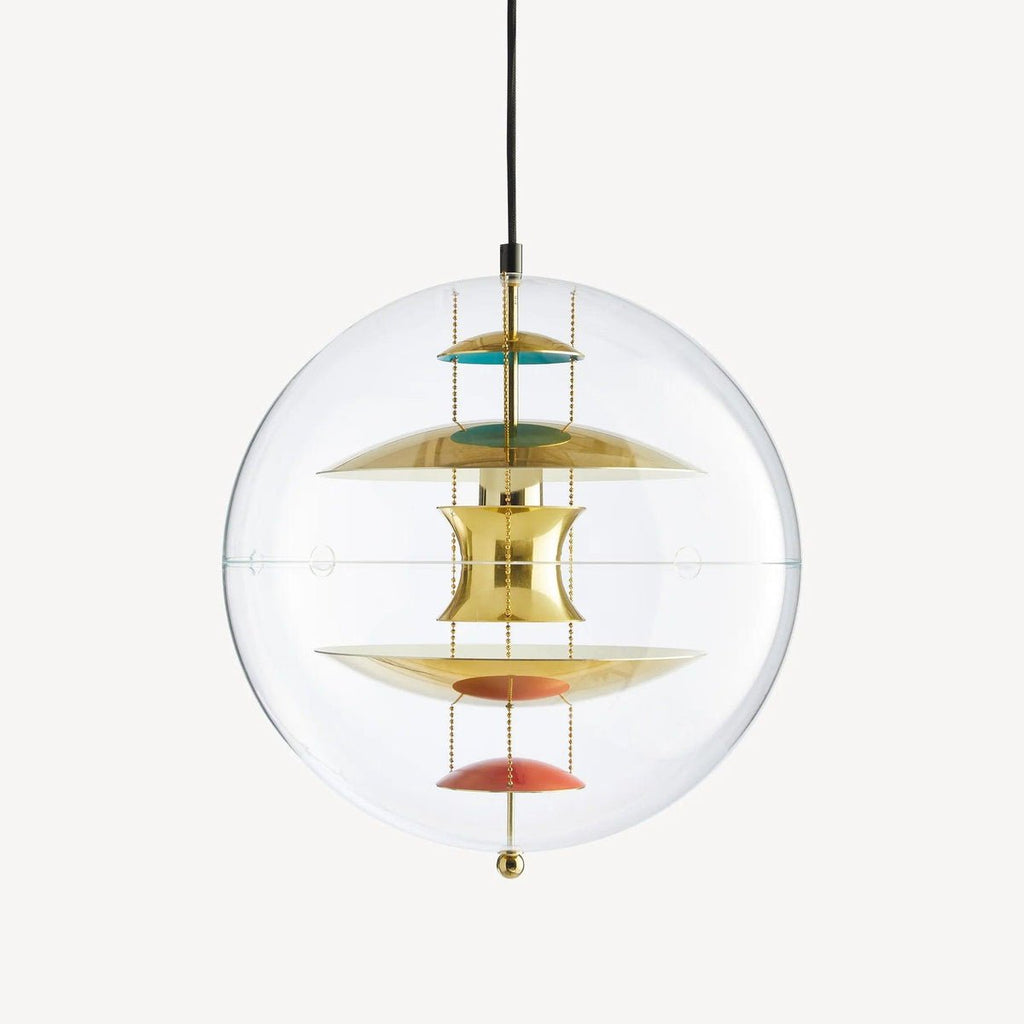 A Clérachic sphere pendant in gold on a plain backdrop, with brass discs, teal and coral dishes and a small brass weight beneath.