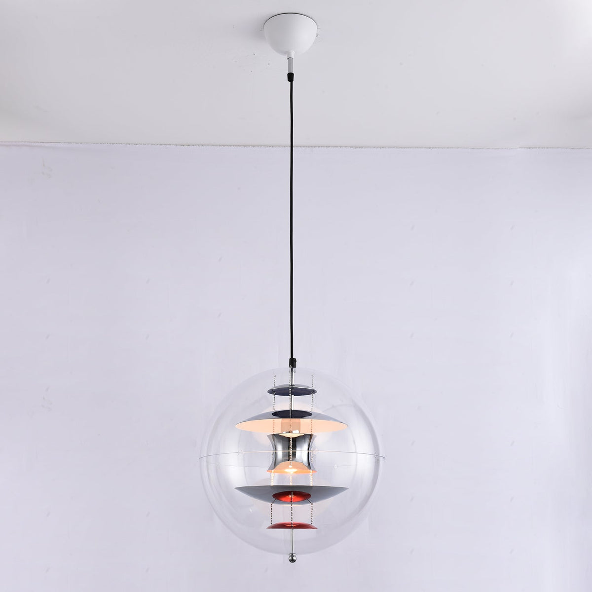 The same chrome-and-red Clérachic sphere pendant, now switched on, with a warm glow lighting the discs inside the acrylic sphere.