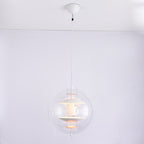 A Clérachic sphere pendant in white with a white cord and canopy, lit with a warm glow inside the clear acrylic sphere.