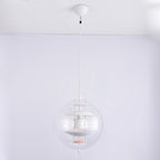 An unlit white Clérachic sphere pendant hangs from a white canopy and white cord against a pale grey-lilac wall.