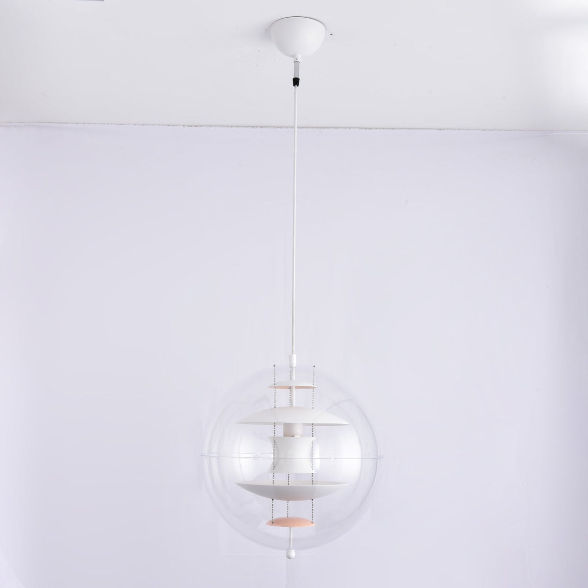 An unlit white Clérachic sphere pendant hangs from a white canopy and white cord against a pale grey-lilac wall.