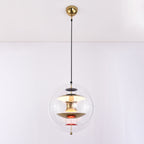 A Clérachic sphere pendant with a gold ceiling canopy and black cord, lit warmly, with brass discs and red dishes inside.