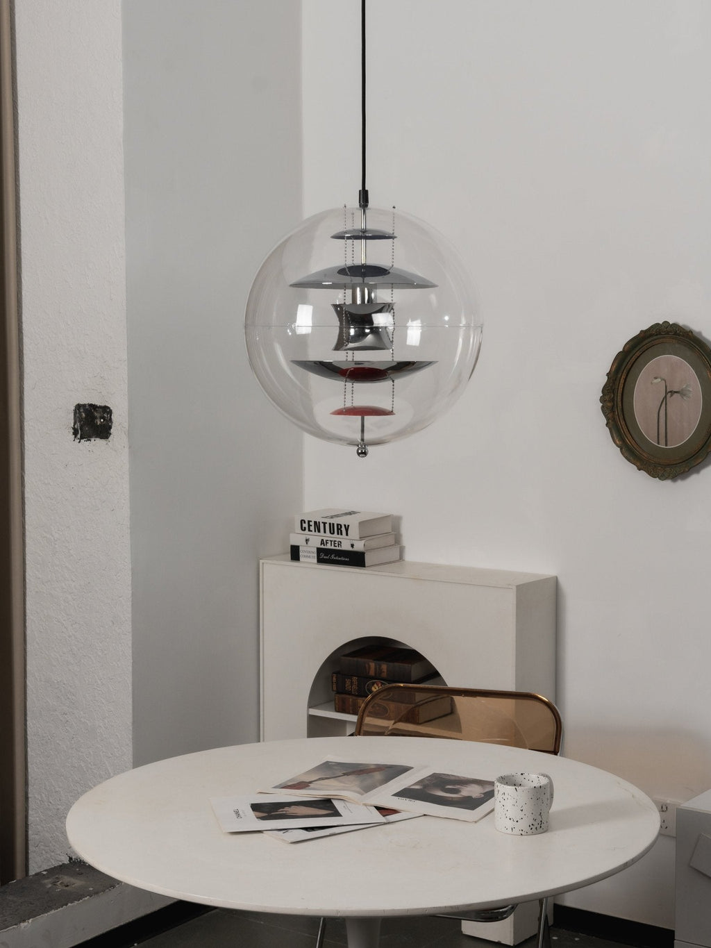 This unlit Clérachic chrome sphere pendant hangs above a white round table, with a round olive-framed mirror on the wall.