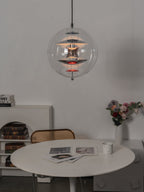 Lit warmly, this chrome Clérachic sphere pendant hangs over a white round table with a posy of flowers and a book shelf behind.