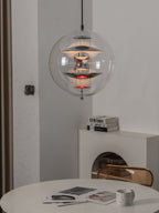 Glowing with a warm light, this Clérachic sphere pendant shows chrome discs and red dishes above a table with magazines and a mug.