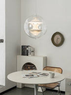 A lit white Clérachic sphere pendant glows softly above a small white round table in a corner with books and a round mirror.