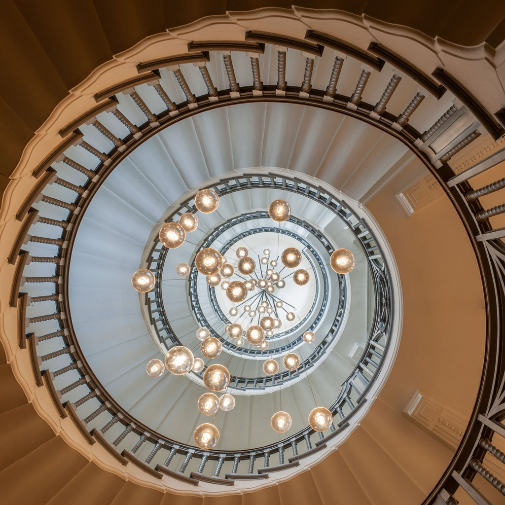 Looking up a spiral staircase, this Clérachic pendant light scatters warm glass spheres down the open well at several heights.