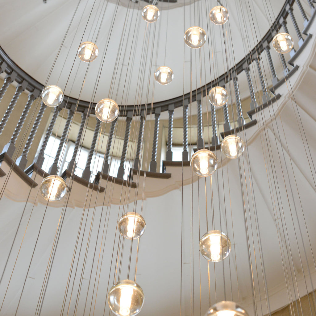 Glass spheres of this Clérachic pendant light glow on long thin cords beside the curving balustrade of a stairwell.