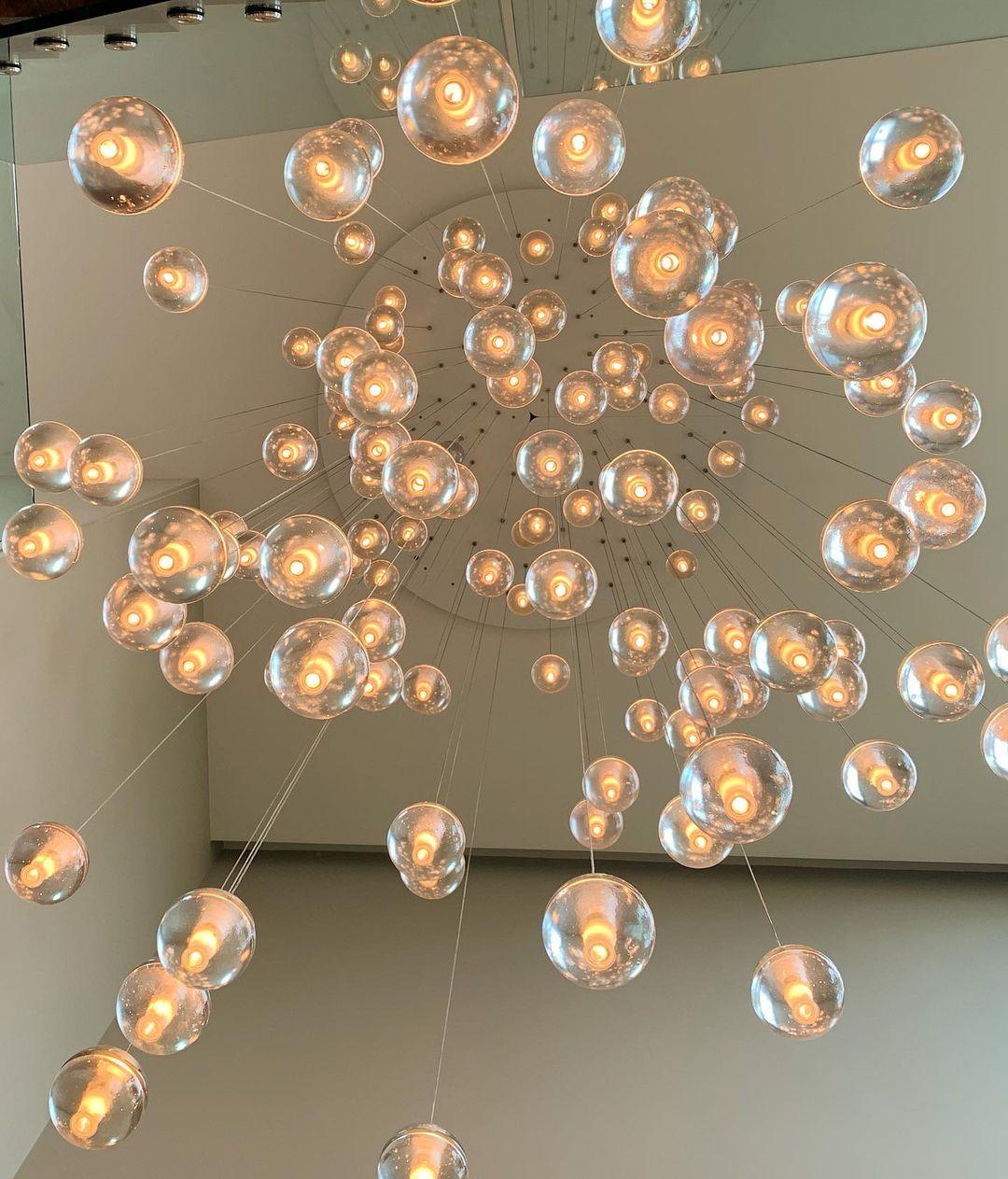 Seen from below, this Clérachic pendant light spreads a spiral of warm glass spheres from the ceiling of a tall white room.