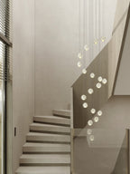 Pale spheres of this Clérachic pendant light trace a slow curve beside a stone staircase with a glass balustrade.