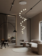 A spiral of lit glass spheres from this Clérachic pendant light drops from a round ceiling plate into a taupe living room.