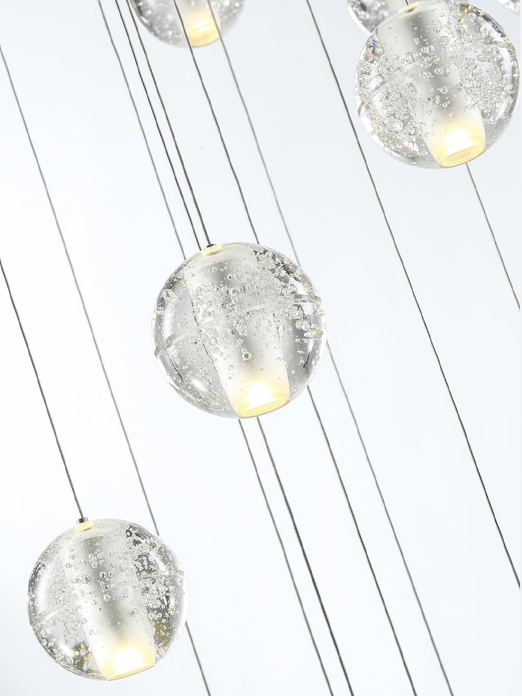 Close view of bubbled clear glass spheres on thin cords from this Clérachic pendant light, a warm glow inside each one.