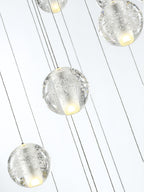 Close view of bubbled clear glass spheres on thin cords from this Clérachic pendant light, a warm glow inside each one.