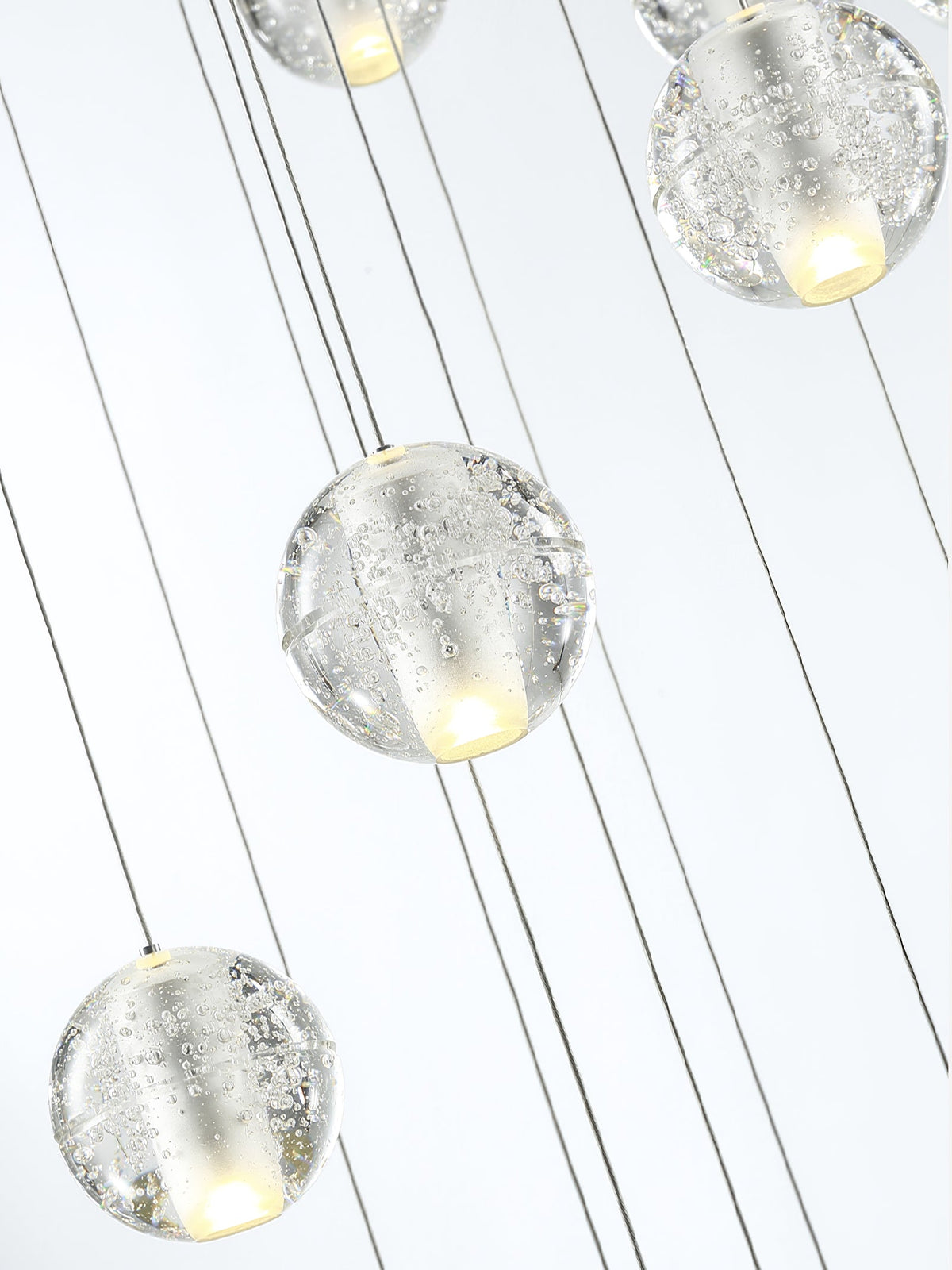 Close view of bubbled clear glass spheres on thin cords from this Clérachic pendant light, a warm glow inside each one.