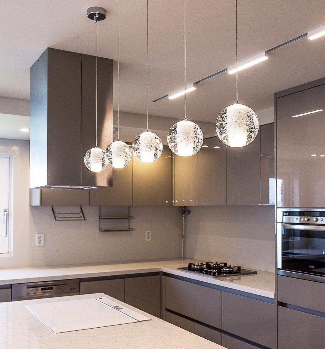 A row of four glass spheres from this Clérachic pendant light hangs at different heights in a grey kitchen under a steel hood.