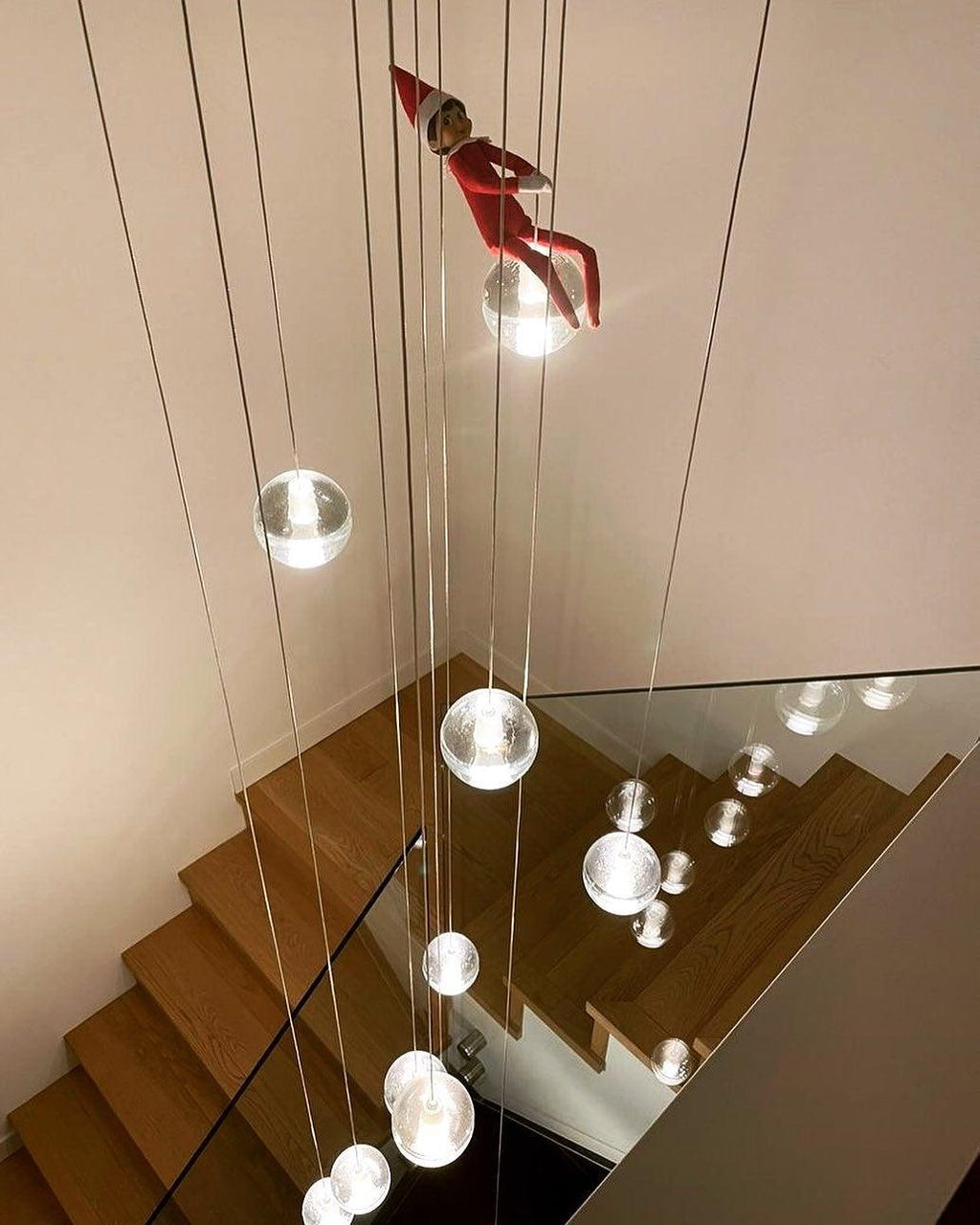 Looking down a timber staircase, spheres from this Clérachic pendant light hang on long cords beside a glass balustrade.