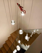 Looking down a timber staircase, spheres from this Clérachic pendant light hang on long cords beside a glass balustrade.