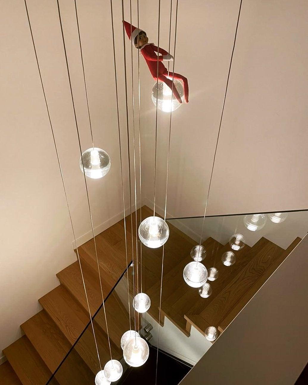 Looking down a timber staircase, spheres from this Clérachic pendant light hang on long cords beside a glass balustrade.
