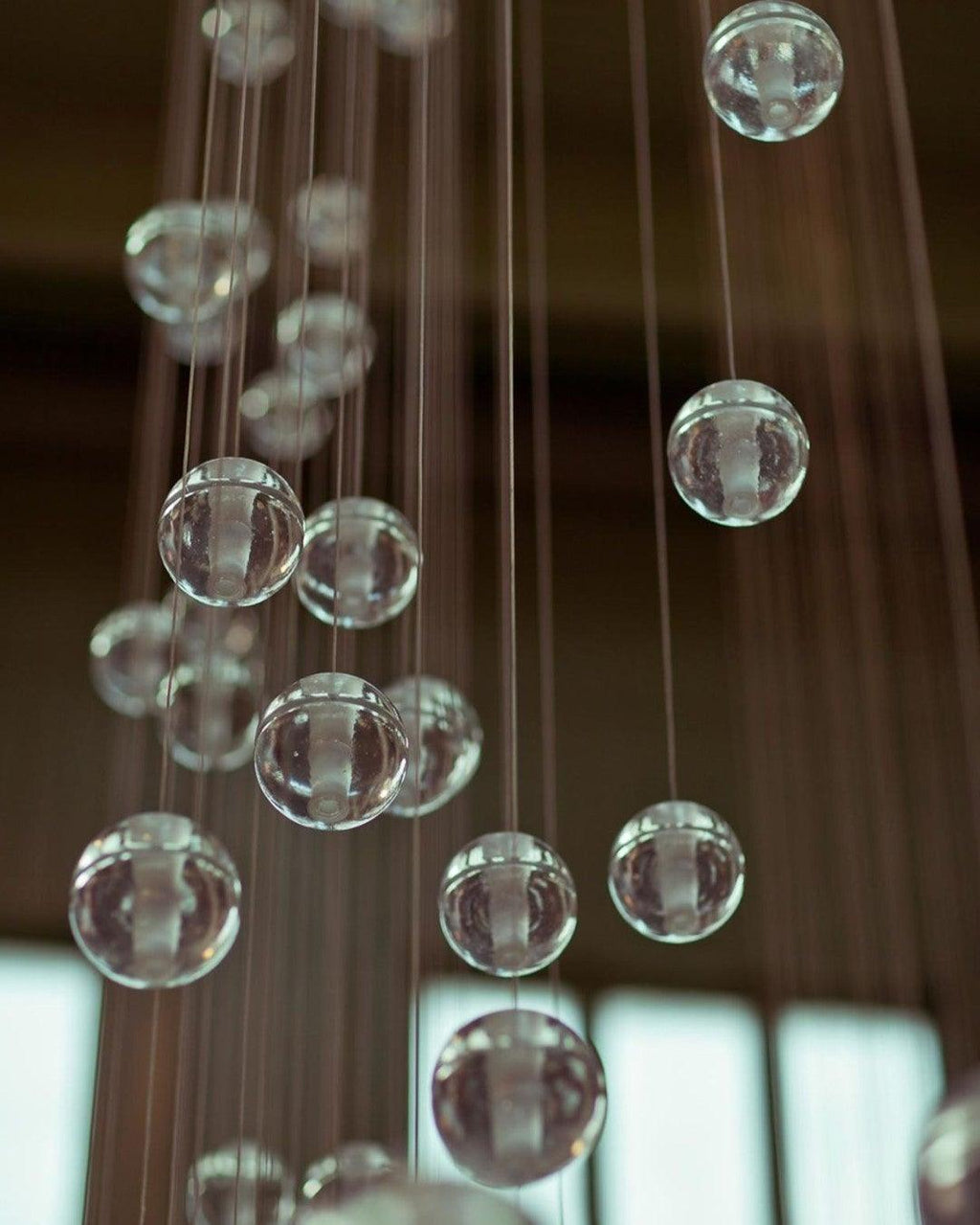 Soft-focus view of clear glass spheres of this Clérachic pendant light hanging on many fine cords in a dark space.