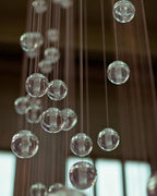 Soft-focus view of clear glass spheres of this Clérachic pendant light hanging on many fine cords in a dark space.