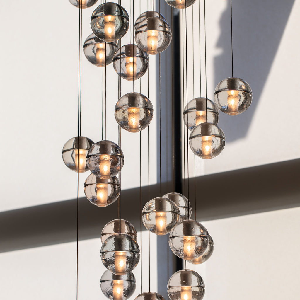 Close view of this Clérachic pendant light's spheres, each with a frosted core and a bright warm glow, against a pale wall.