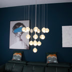 In a living room with a deep blue wall and green leather sofa, this Clérachic pendant light hangs a lit cluster of spheres.