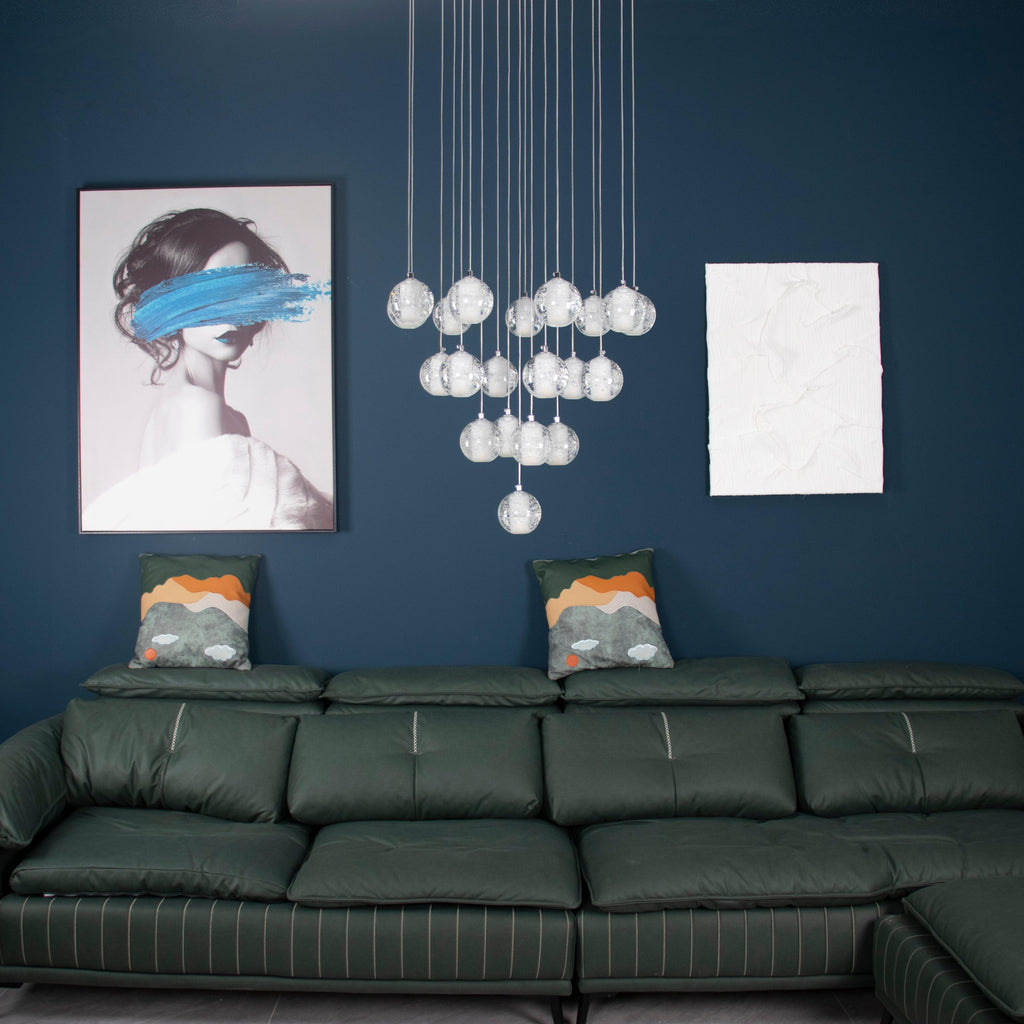 Unlit, the spheres of this Clérachic pendant light hang above a green leather sofa and a framed portrait on a blue wall.