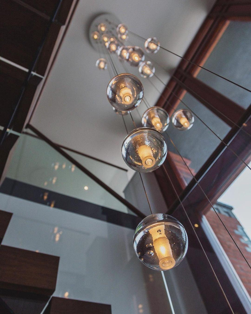 Looking up past a glass balustrade, this Clérachic pendant light hangs lit spheres from a round ceiling plate on angled cords.