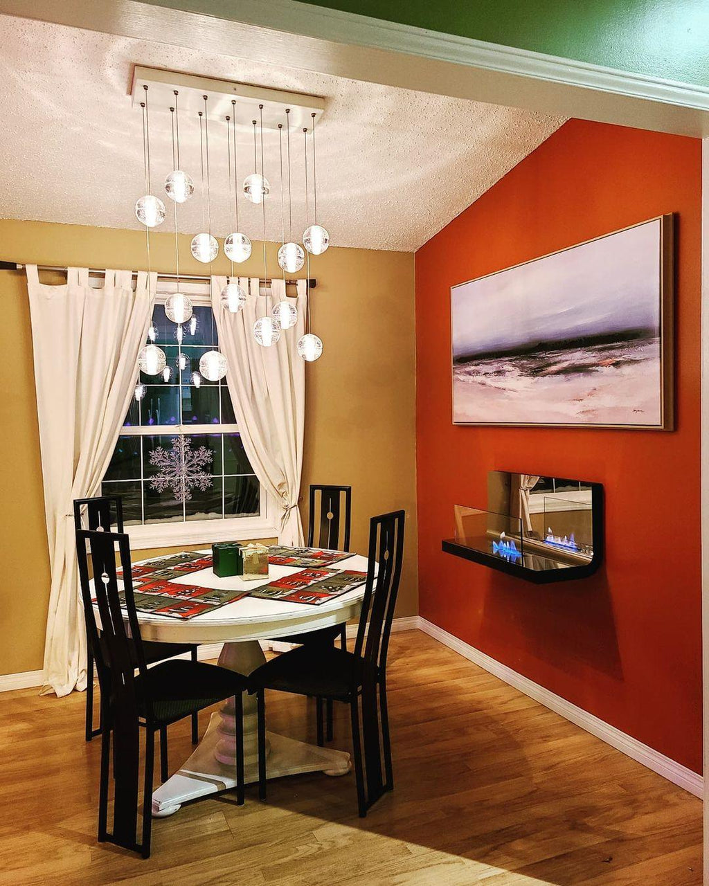 Over a round dining table in a room with an orange wall, this Clérachic pendant light hangs spheres from a long rectangular canopy.