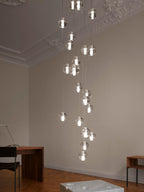 A column of lit glass spheres from this Clérachic pendant light drops through a tall, ornate-ceilinged room to a wooden desk below.