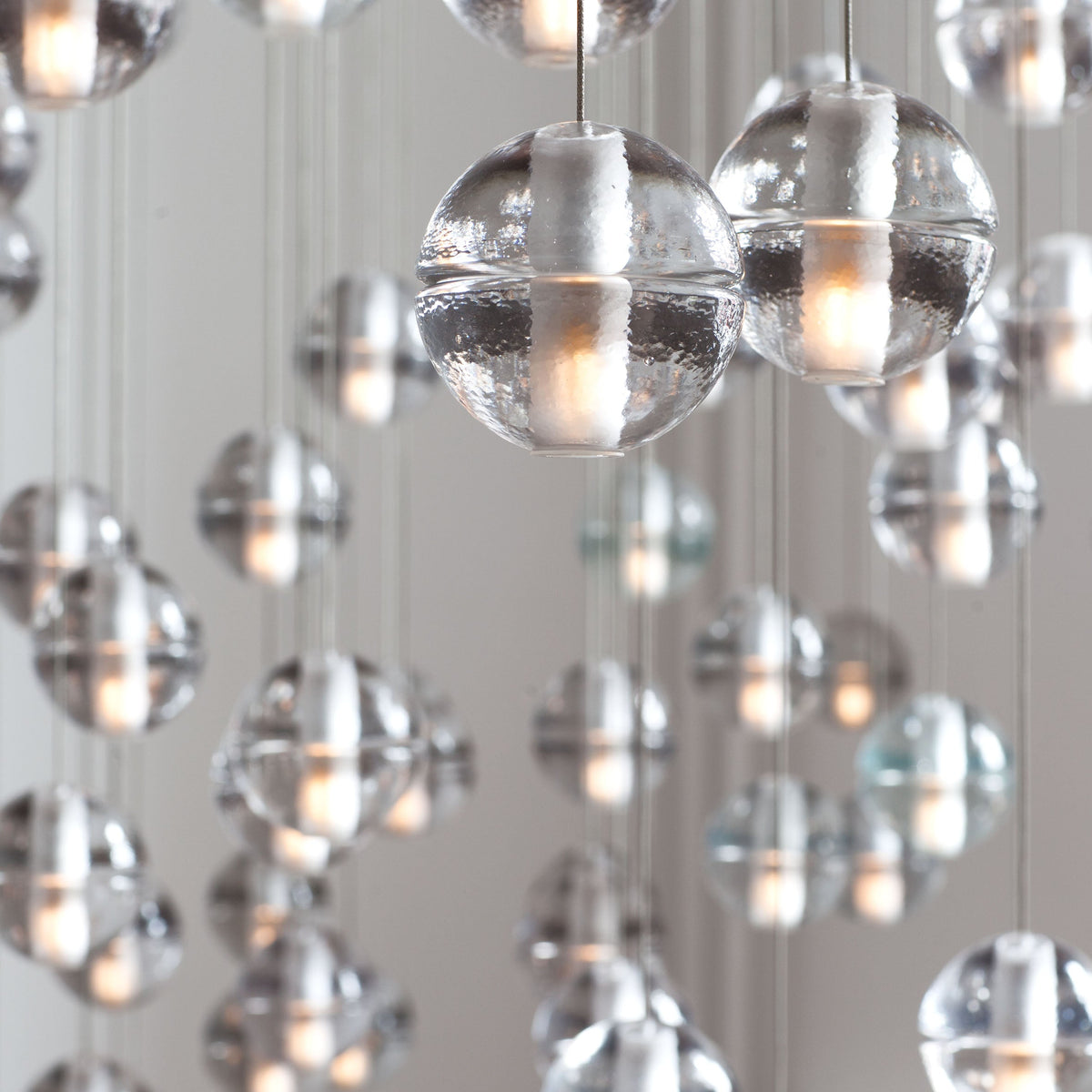Close view of two clear glass spheres on this Clérachic pendant light, each with a frosted inner core and a warm glow.
