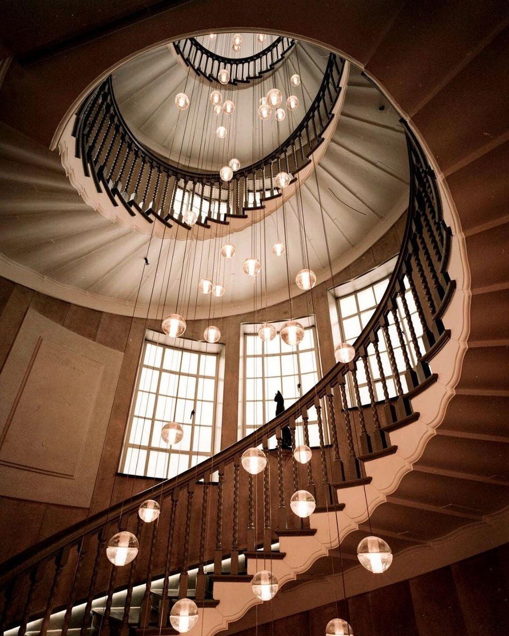 Looking down a spiral staircase, this Clérachic pendant light scatters lit spheres in the stairwell beside tall windows.