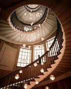 Looking down a spiral staircase, this Clérachic pendant light scatters lit spheres in the stairwell beside tall windows.