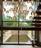Lit spheres from this Clérachic pendant light hang in front of a glazed wall that looks out onto a garden and a still pool.