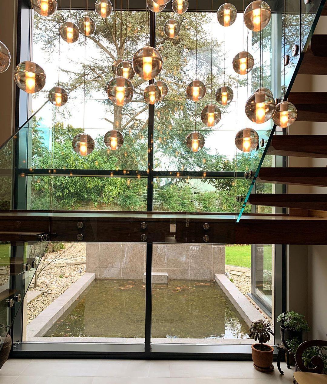 Lit spheres from this Clérachic pendant light hang in front of a glazed wall that looks out onto a garden and a still pool.