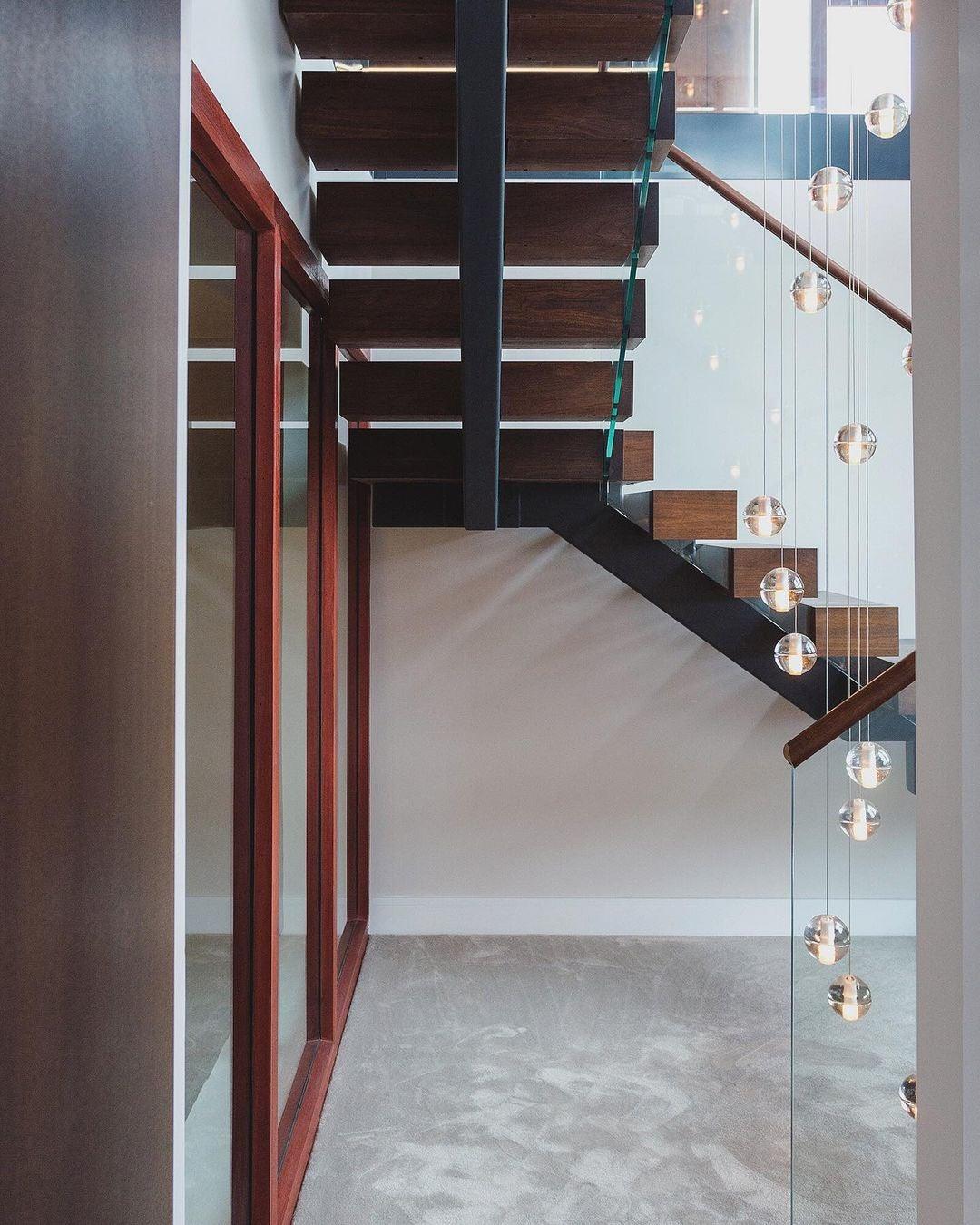 A trail of small glass spheres from this Clérachic pendant light hangs past a floating timber staircase and a glass wall.