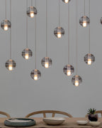 Clear glass spheres of this Clérachic pendant light hang over a long wooden table set with bowls, with wishbone chairs below.