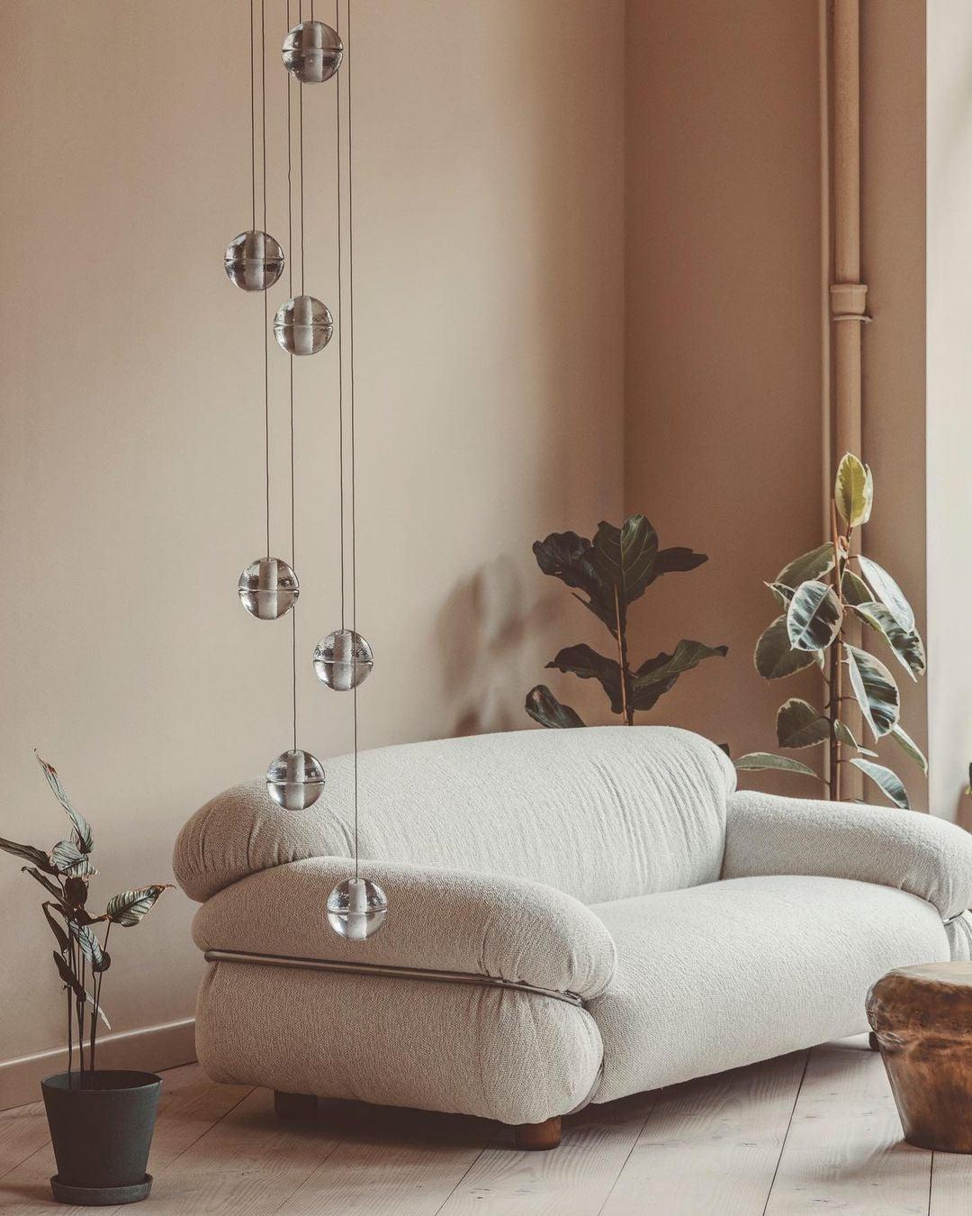 A short string of glass spheres from this Clérachic pendant light hangs above a cream bouclé sofa and two leafy plants.