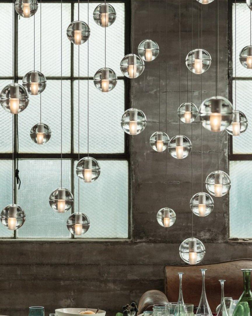 Clear spheres of this Clérachic pendant light hang at varied heights before a frosted industrial window, with glassware below.