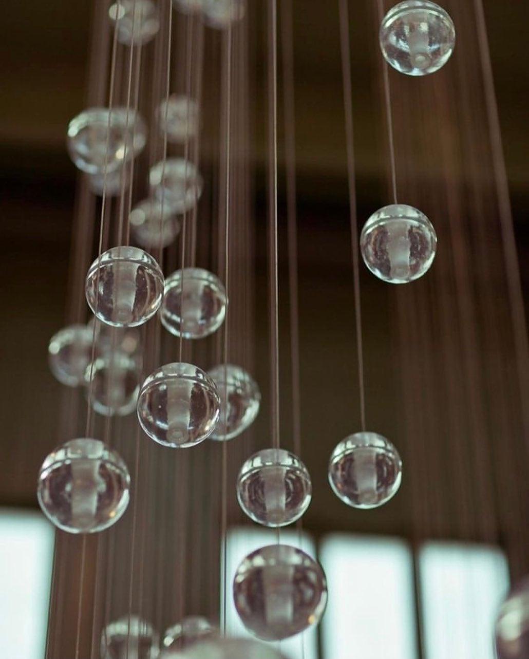 Out-of-focus glass spheres of this Clérachic pendant light on thin cords against a dark wood background.