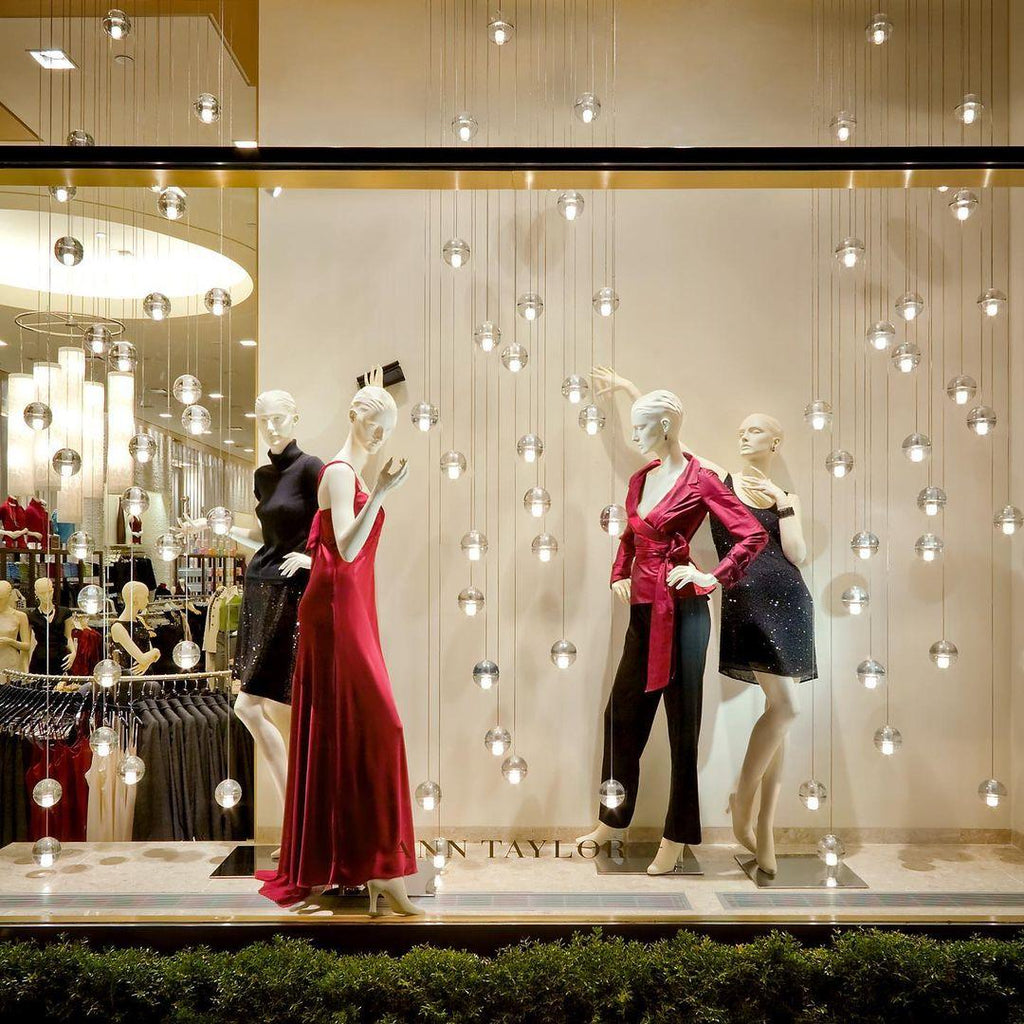 Small glass spheres of this Clérachic pendant light hang in a boutique window around mannequins in red and dark dresses.