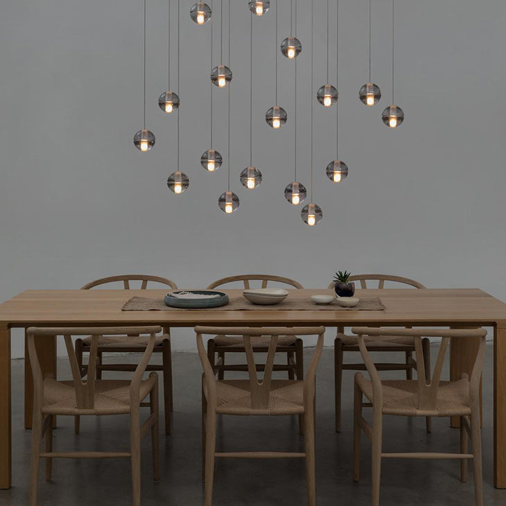 Two dozen small glowing spheres from this Clérachic pendant light hang above a pale oak dining table with wishbone chairs.