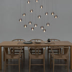 Two dozen small glowing spheres from this Clérachic pendant light hang above a pale oak dining table with wishbone chairs.