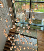 A dense fall of warm spheres from this Clérachic pendant light hangs through a stairwell, with a garden seen through glass behind.
