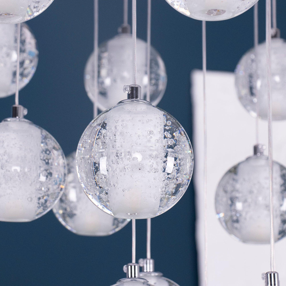 Close view of bubbled clear glass spheres from this Clérachic pendant light, each with a frosted inner core, on a deep blue wall.