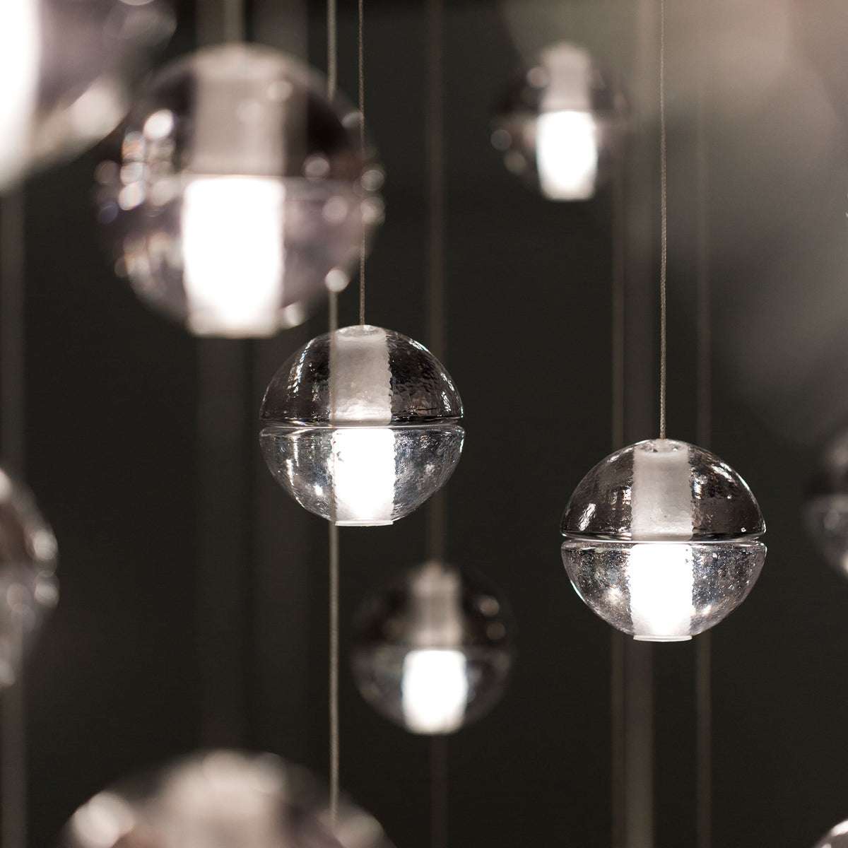 Warm light glows inside the frosted cores of clear glass spheres from this Clérachic pendant light, against a dark background.