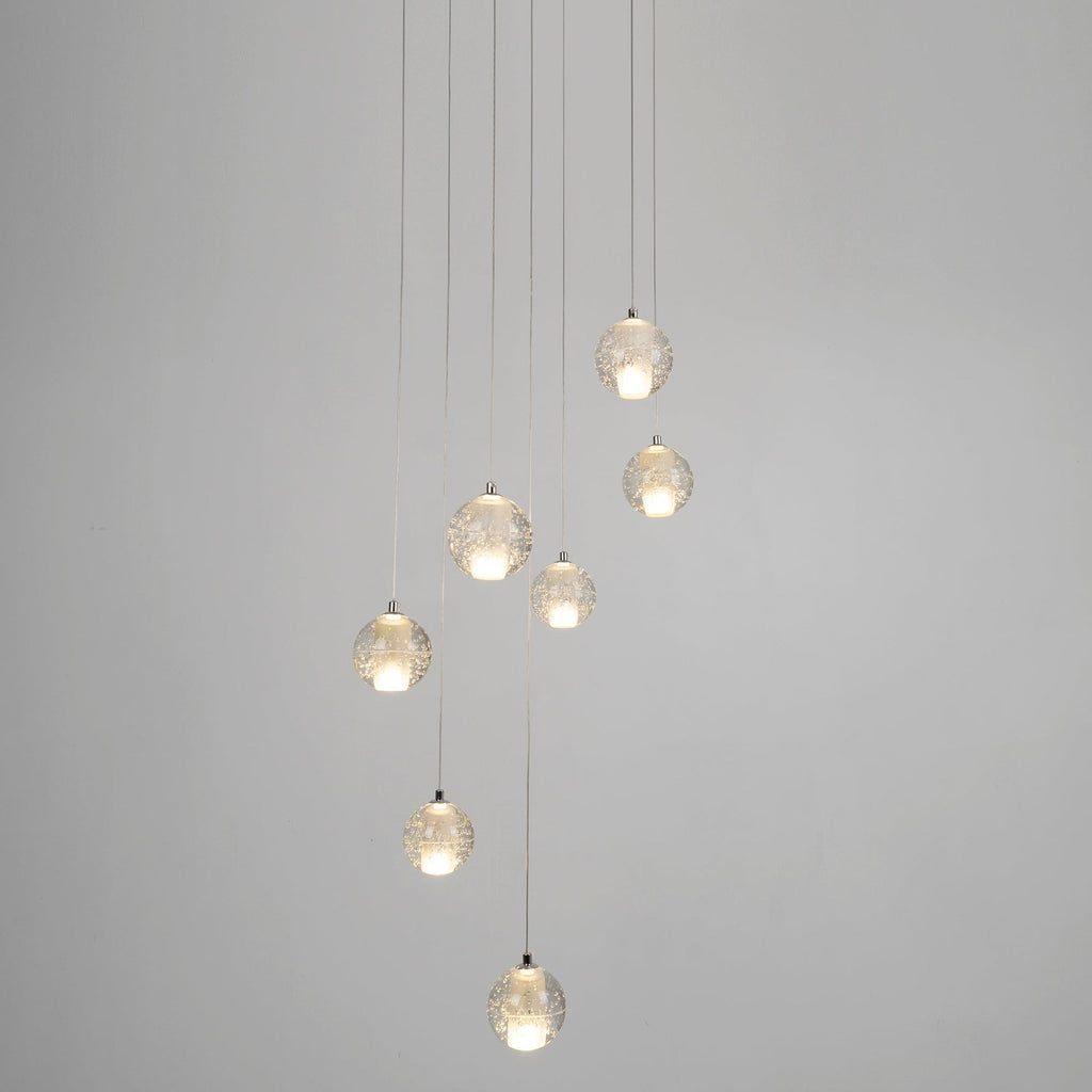Eight spheres from this Clérachic pendant light hang on long cords at different heights against a plain grey wall.